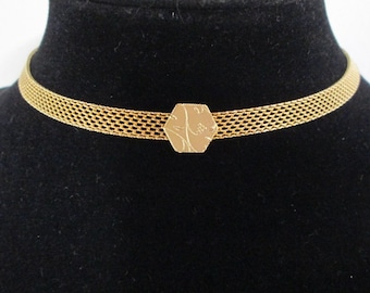 May include: A gold-toned choker necklace with a mesh chain and a hexagonal pendant with a floral design.