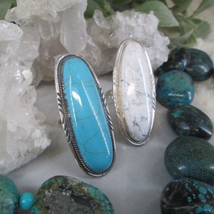 May include: Two silver rings with oval-shaped turquoise and white stones. The rings are set against a background of white quartz crystals and turquoise stones.