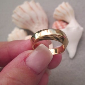 May include: A gold-colored ring with a smooth, rounded surface. The ring is slightly wider on one side, giving it a unique, asymmetrical design.