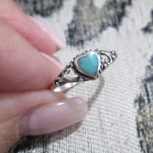 May include: A silver ring with a heart-shaped turquoise stone. The ring has a delicate design with swirls and curves.