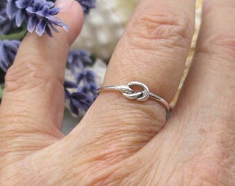 May include: A simple silver knot ring on a finger.