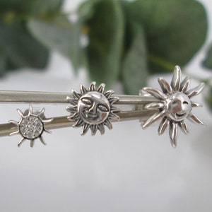 May include: Three silver sun earrings with different designs. One sun has a face, one has a face and a circle of small stones, and one is a simple sun with rays.