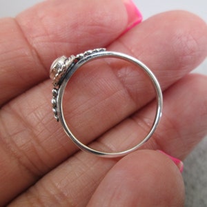 May include: A silver ring with a small, clear stone set in a beaded band.