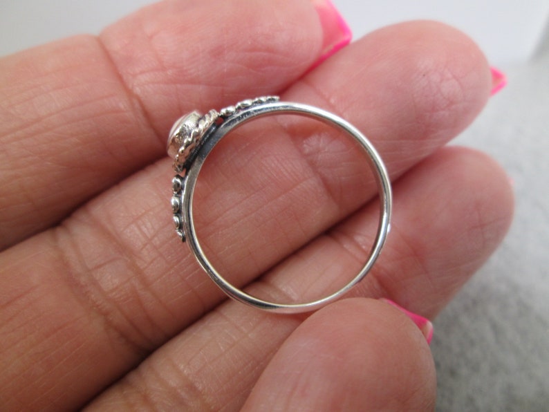 May include: A silver ring with a small, clear stone set in a beaded band.