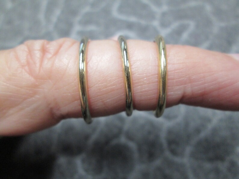 May include: Three gold-colored metal rings stacked on a finger.