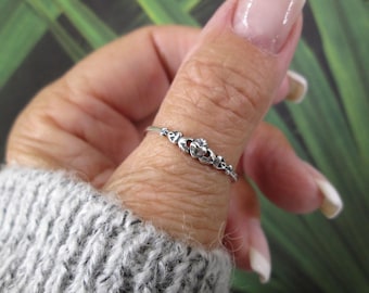 May include: A thin silver Claddagh ring featuring a central heart held by two hands and topped with a small crown. The band is slender and metallic, showcasing the traditional Irish design elements in a polished, reflective silver finish.