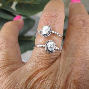May include: Two silver rings with white oval stones set in a beaded bezel. The rings are worn on a finger.