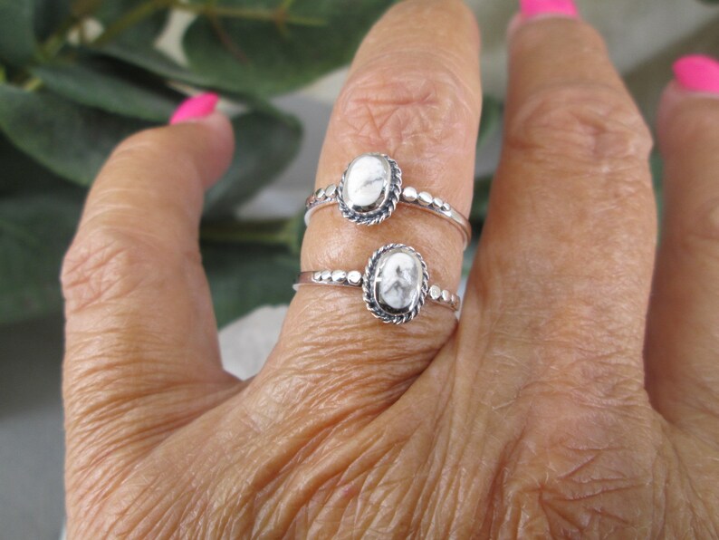 May include: Two silver rings with white oval stones set in a beaded bezel. The rings are worn on a finger.