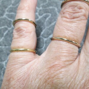 May include: A hand wearing four thin gold rings on different fingers.