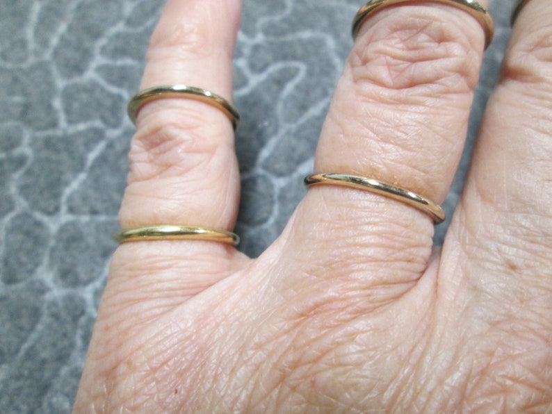 May include: A hand wearing four thin gold rings on different fingers.