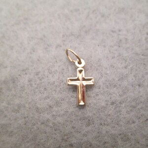 May include: A small gold cross charm pendant. The cross has a simple design with a slightly raised center.