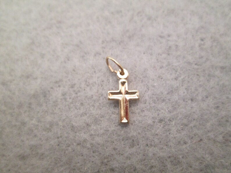 May include: A small gold cross charm pendant. The cross has a simple design with a slightly raised center.