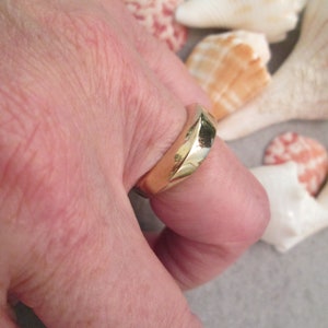 May include: A gold band ring with a unique, angular design. The ring is worn on a person's finger.