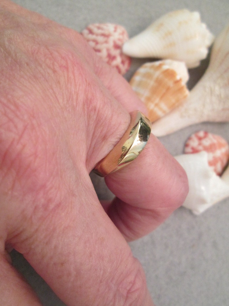 May include: A gold band ring with a unique, angular design. The ring is worn on a person's finger.