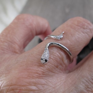 May include: A silver snake ring with black and white cubic zirconia stones. The snake is coiled around the finger and the head is facing forward.