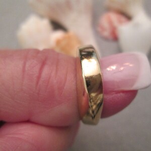 May include: A gold band ring worn on a finger.