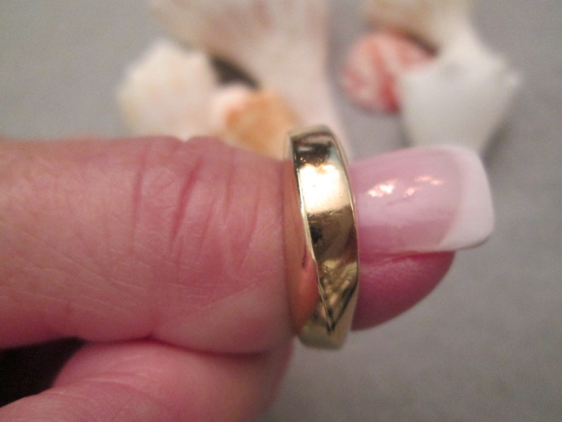 May include: A gold band ring worn on a finger.