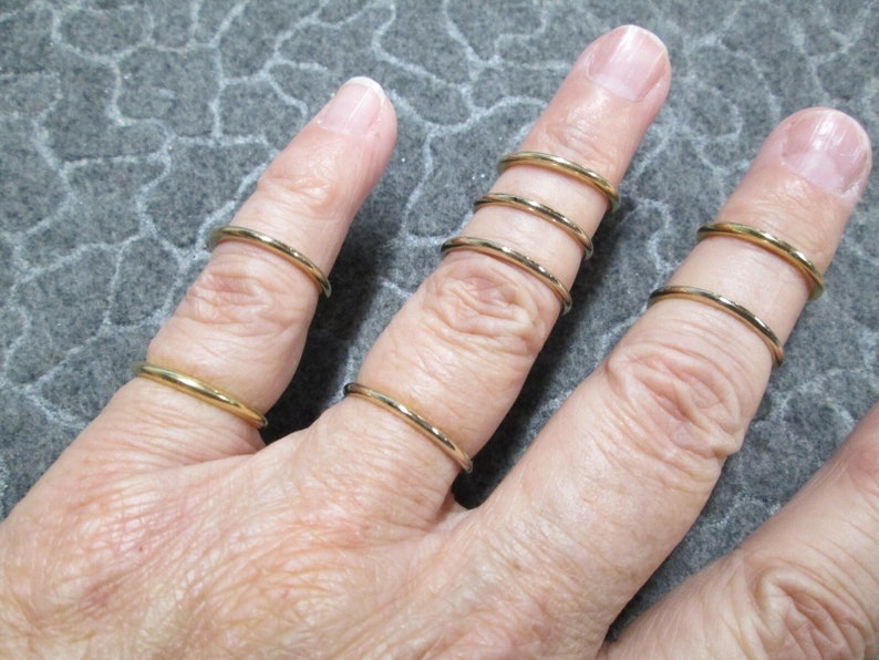 May include: A set of five gold-toned stacking rings. The rings are thin and delicate, and they are worn on a finger.