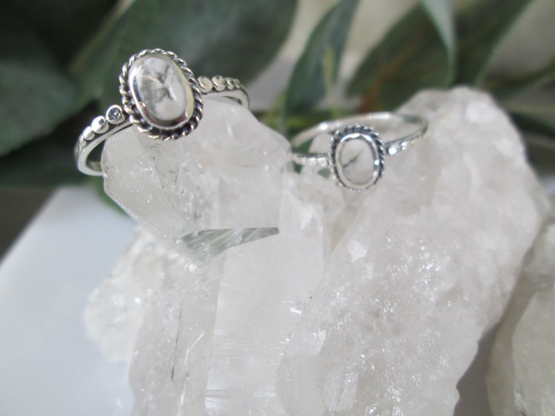 May include: Two silver rings with oval-shaped white stones set in a silver bezel. The rings are on a bed of white crystal rocks.