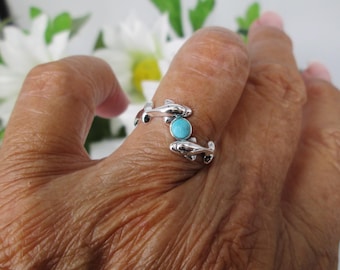 Puede incluir: Anillo de plata con dos figuras de delfines y una piedra turquesa en el centro. El anillo, que se lleva en un dedo, presenta un diseño de temática oceánica. Una pieza de joyería única y original.