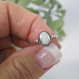May include: A silver ring with a white opal gemstone set in a beaded bezel. The ring is on a finger.