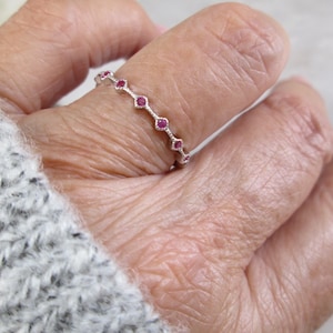 May include: A silver ring with a row of small, pink gemstones. The ring is on a person's finger.