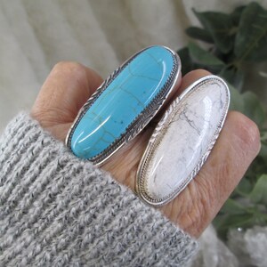 May include: Two silver rings with oval-shaped turquoise and white stones. The rings are worn on a person's fingers.