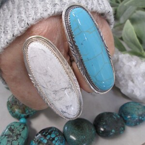 May include: Two silver rings with oval-shaped turquoise stones. The ring on the left has a white stone, while the ring on the right has a blue stone.