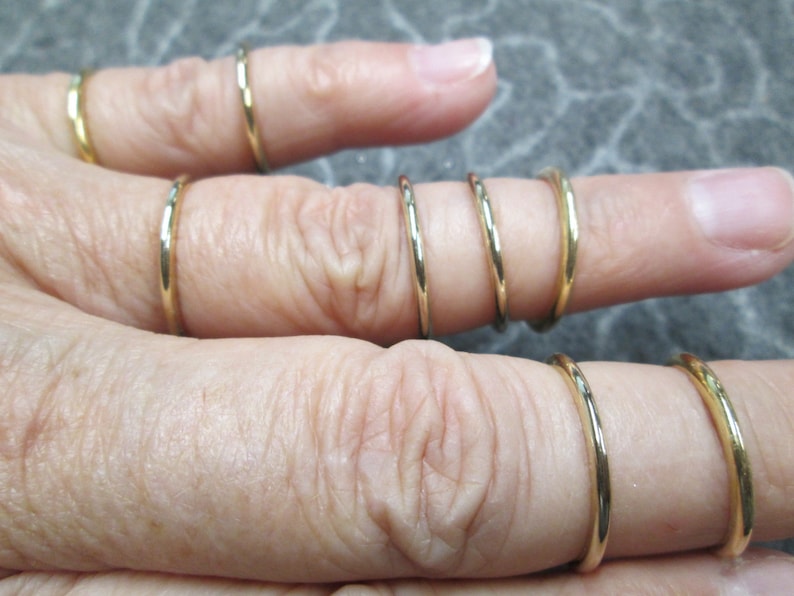 May include: A set of five gold-toned stacking rings. The rings are thin and delicate, and they are worn on a finger.