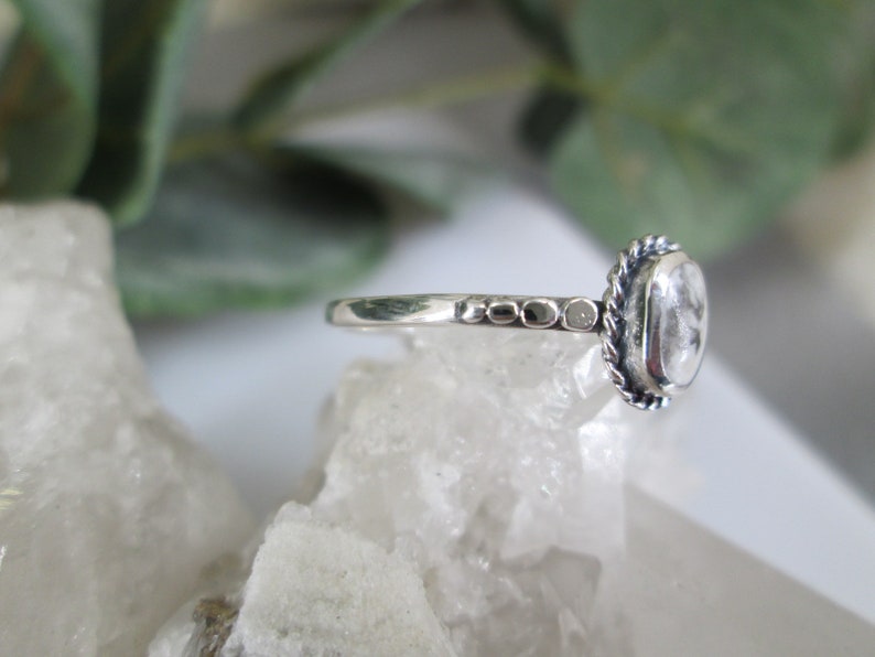 May include: A silver ring with a clear gemstone set in a rope-like bezel. The band is textured with small beads.