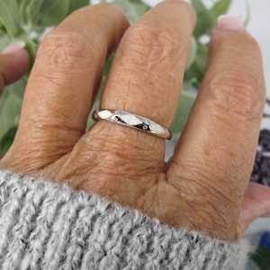 May include: A silver ring with a geometric design and small, clear gemstones. The ring is worn on a finger, showcasing its polished finish and delicate details. The ring's design is a band with alternating facets and small gemstones.