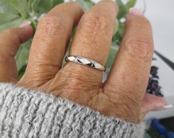 Puede incluir: Un anillo plateado con un diseño geométrico y pequeñas gemas transparentes. El anillo se lleva en un dedo, mostrando su acabado pulido y detalles delicados. El diseño del anillo es una banda con facetas alternas y pequeñas gemas.