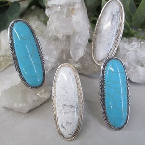 May include: Four oval-shaped rings with silver settings and turquoise or white stones. The rings are displayed on a white background.