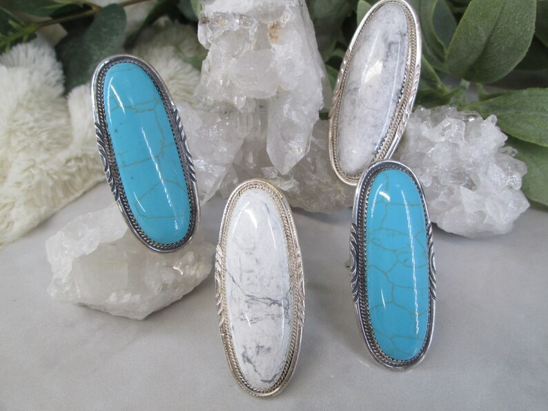 May include: Four oval-shaped rings with silver settings and turquoise or white stones. The rings are displayed on a white background.