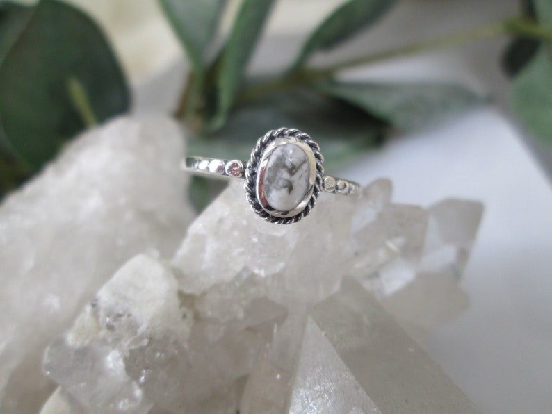 May include: A silver ring with a white oval-shaped stone set in a rope-like border.