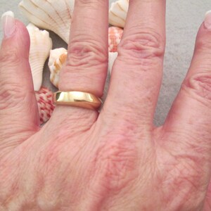 May include: A close-up of a person's hand wearing a gold wedding band. The ring is simple and has a smooth, polished finish.