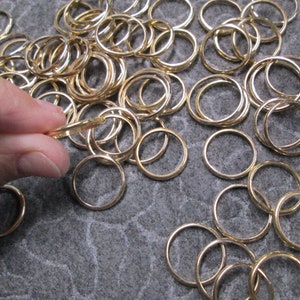 May include: A large pile of gold-colored metal jump rings. The rings are of various sizes and are arranged in a random pattern.