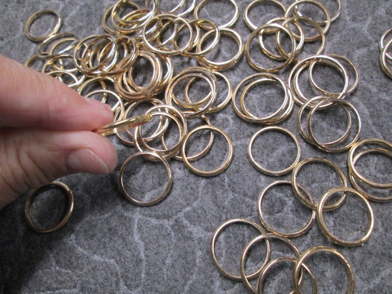 May include: A large pile of gold-colored metal jump rings. The rings are of various sizes and are arranged in a random pattern.