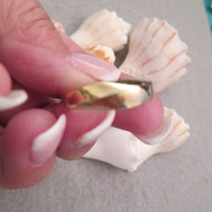 May include: A simple gold band ring with a slightly rounded edge.