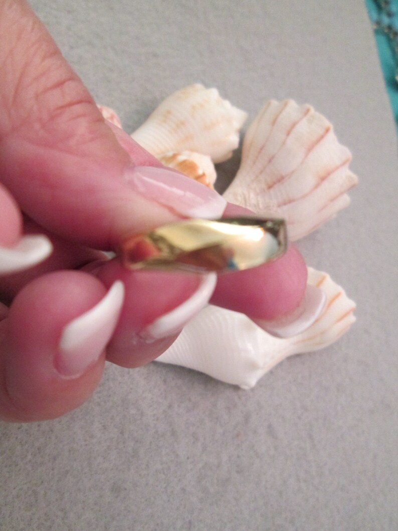 May include: A simple gold band ring with a slightly rounded edge.