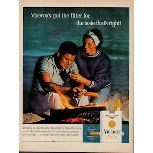 May include: Vintage advertisement for Viceroy cigarettes. A man and woman are seated near a campfire on a beach. The ad features the Viceroy cigarette pack with the text "Viceroy's got the filter for the taste that's right!"