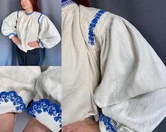 May include: A white linen blouse with blue embroidered details. The blouse has a round neckline and long, puffy sleeves. The embroidery is a floral pattern.