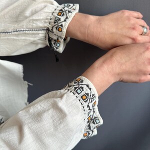 May include: White linen blouse with embroidered cuffs featuring a geometric pattern in black, orange, and blue.