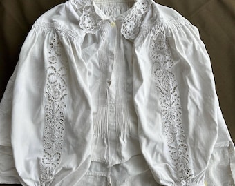 May include: A white cotton blouse with a lace collar and cuffs. The lace is intricate and delicate, and the blouse has a vintage look.