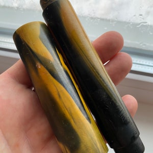 May include: Two black and yellow striped pen barrels. The barrels are made of a marbled plastic material.