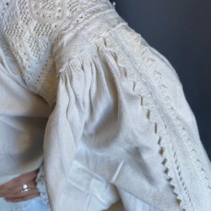 K&ouml;nnte beinhalten: Wei&szlig;e Leinenbluse mit zarter Stickerei an Ausschnitt und &Auml;rmeln. Die Stickerei ist ein traditionelles Muster mit wei&szlig;em Garn.