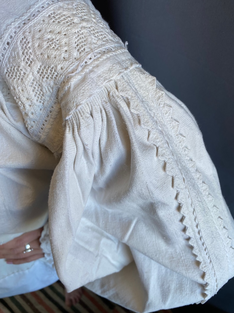 K&ouml;nnte beinhalten: Wei&szlig;e Leinenbluse mit zarter Stickerei an Ausschnitt und &Auml;rmeln. Die Stickerei ist ein traditionelles Muster mit wei&szlig;em Garn.