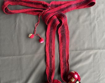 May include: A red and black woven belt with tassels and pom-poms. The pom-poms are red, white, and green.