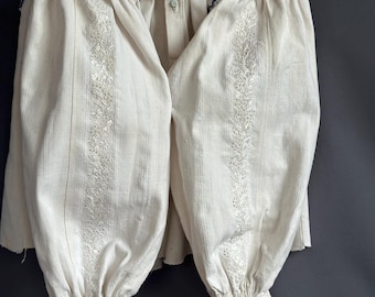 May include: A white linen shirt with delicate embroidery and lace trim. The shirt has a button-up front and long sleeves with gathered cuffs.
