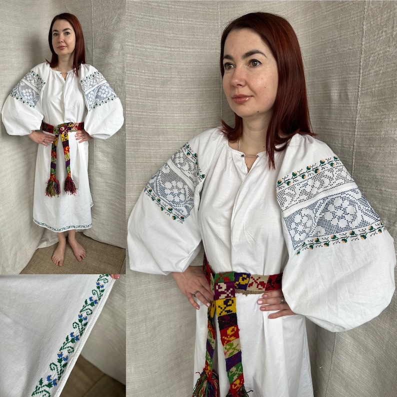 May include: A white linen dress with embroidered sleeves and a colorful woven belt. The dress has a round neckline and long sleeves. The embroidery on the sleeves is a floral pattern with green and blue accents. The belt is a multi-colored woven design with tassels.